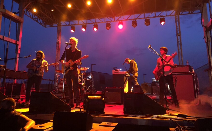 Rock band Spoon performing on a stage with dark blue cloudy sky behind them.