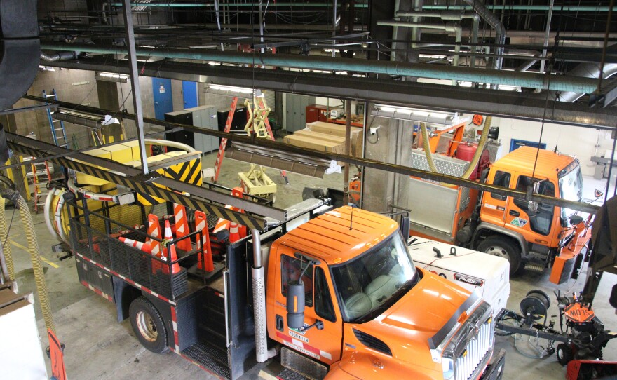 One big orange truck and one small orange truck are parked in a garage.