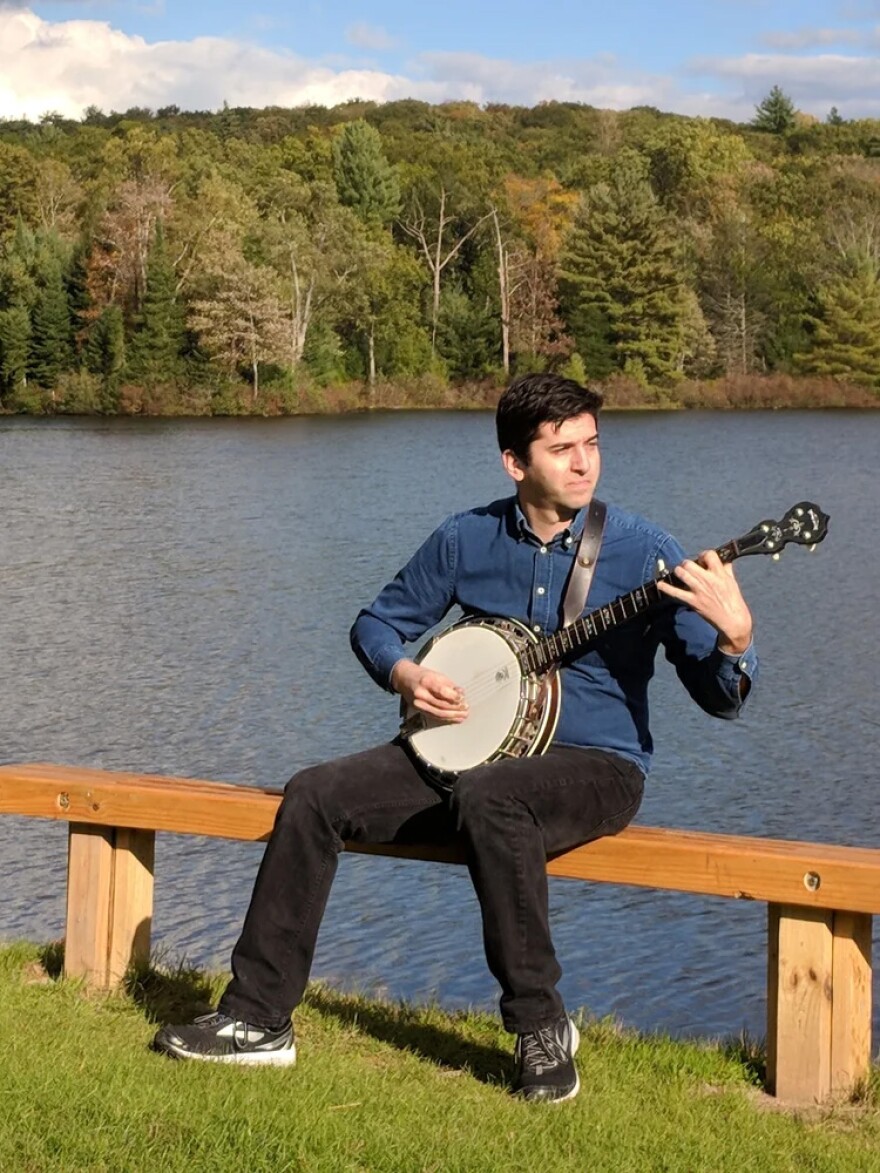 Picture of FOIA Love creator Curtis Raye on bench in front of a lake with a banjo