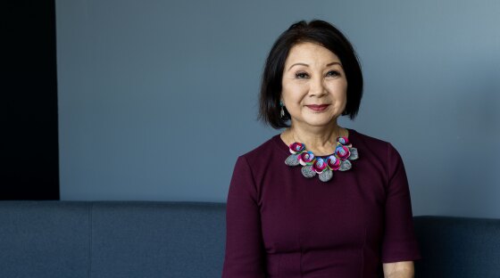 A woman in a dark plum dress sits on a couch. 