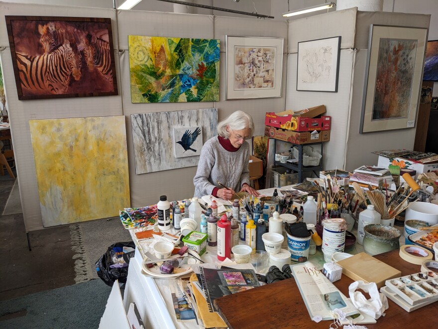 Woman painting in her studio on a large art table covered with painting materials
