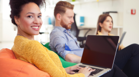 A woman sitting on a bean bag with her hands resting on a laptop, that has the screen turned off. 