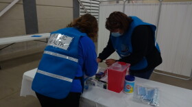 File photo - Two Kalamazoo County health department nurses wearing blue vests bend over a work table as they prepare Pfizer COVID vaccine doses for a mass-vaccination clinic at the Kalamazoo County Expo Center on December 22