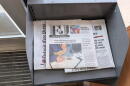 The Flint Journal sits on top of a copy of The Detroit News and the Detroit Free Press in a grey, metal newsstand