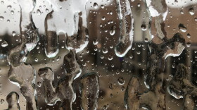 Close up view of ice and water on a glass window, with blurred view of buildings in the background