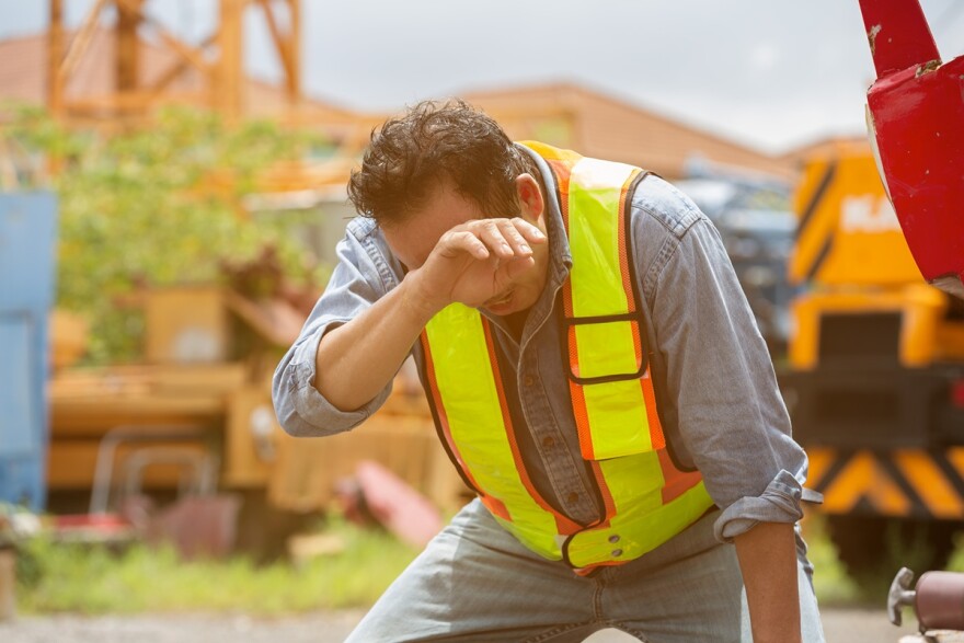 male construction worker leans over and wipes sweat from his face