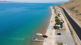 An aerial photo of a road and parking area with cars and boats next to a large blue lake.