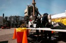 Two people in protective gear with tanks on their back stand with an industrial site in the distance.