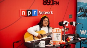 Samara Jane, winner of the 2025 Highway 309 Studio Sessions Contest, performs at WGLT. She sits in front of a red WGLT and NPR Network backdrop, playing an acoustic guitar and singing into a studio microphone, with a keyboard and radio gear on the table in front of her.