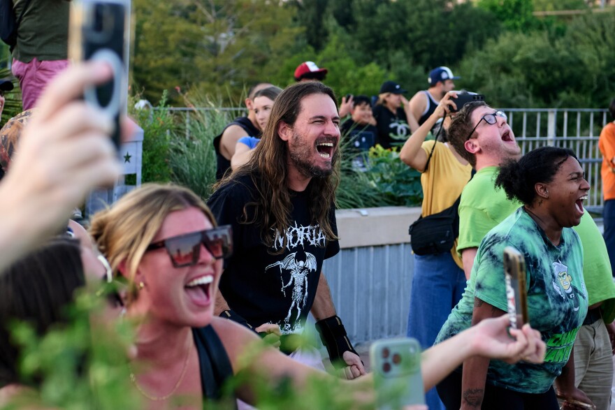 Gustavo Seixas screams, while surrounded by other people screaming and taking photos.