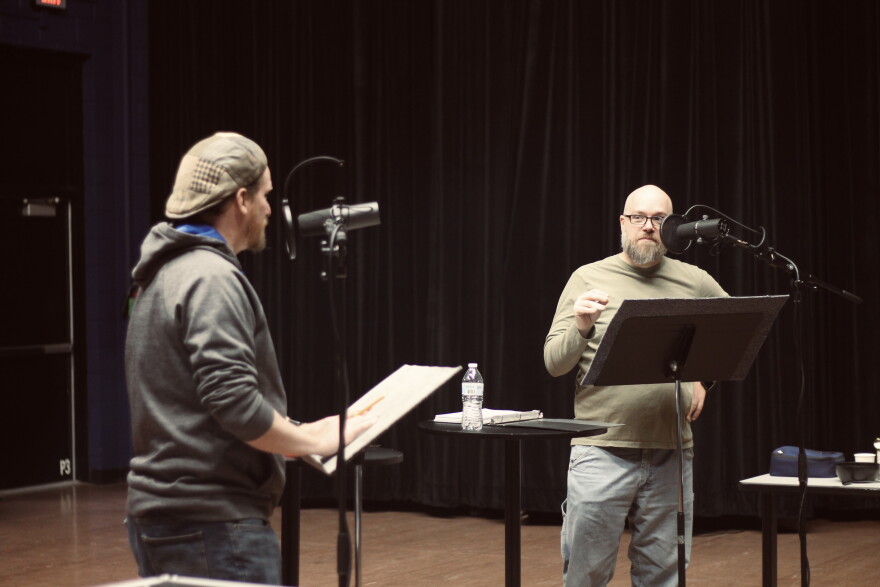 Two men stand and talk in front of podiums and mics.