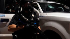 A Denver police officer stands in front of a police truck  with a shattered window in Denver, Colorado  during a protest over the death of George Floyd, an unarmed black man who died while while being arrested and pinned to the ground by the knee of a Minneapolis police officer.