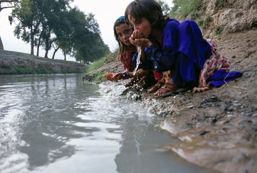 Young girls drink water from a canal flowing between nearby refugee camps and the main road in Peshawar, Pakistan.