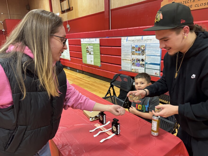 A teenager sprays a perfume onto a person's wrist at an event in a gymnasium.
