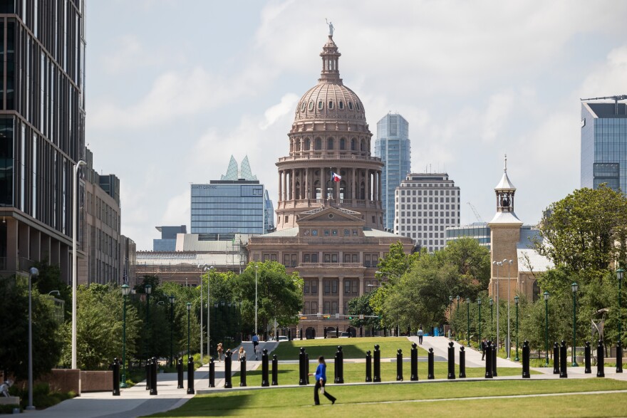 People walk on a stretch of grass in front of the Texas Capitol building.