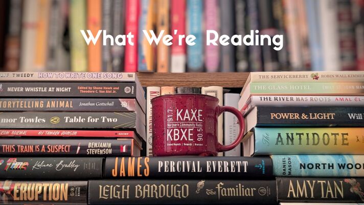 books and a mug with KAXE on it. Text reads "What We're Reading"