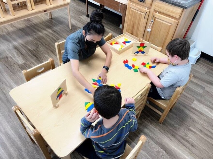 A photo of a woman teaching two children at desk. 