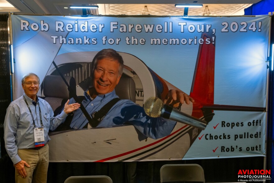 Rob Reider stands in front of a banner saluting his last year announcing air shows.