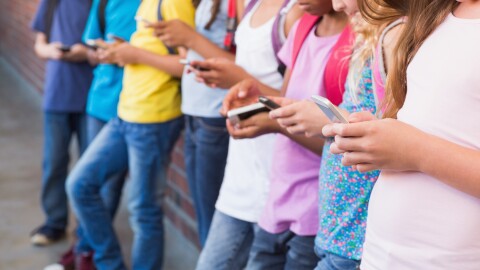 Kids using mobile phones at an elementary school. Stock photo.