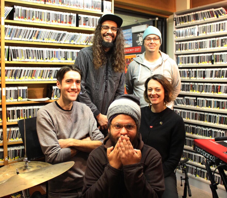 Five people standing together in front of a wall of CDs