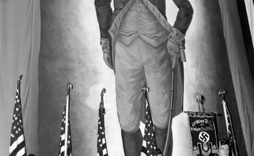 A color guard holding American flags and a banner inscribed with the Nazi swastika stands before an immense portrait of George Washington at the German American Bund's rally at Madison Square Garden.