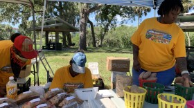 Three African-American women in yellow T-shirts tend to  table at the Newtown farmers market