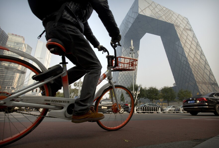 A man rides a Mobike bicycle past the CCTV Headquarters building in Beijing.