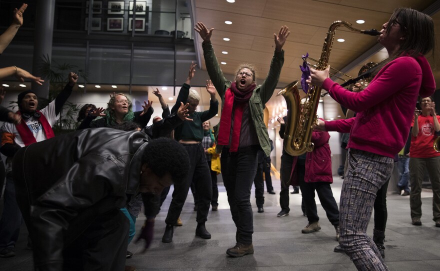 Davis Shoulders, center, dances as Rise Up! Action Band member Adrienne Kerr plays the saxophone on Wednesday, November 1, 2017, during a rally at City Hall in Seattle. 