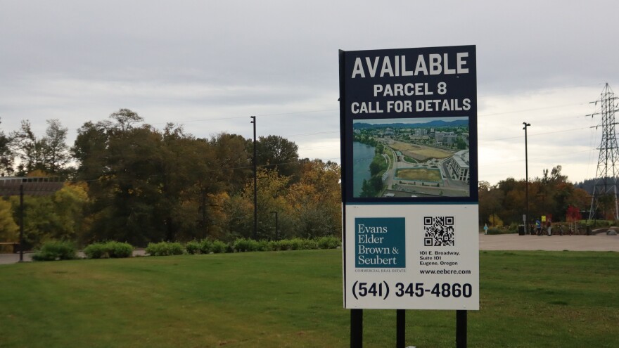 A real estate sign sitting on a grass field in front of trees.