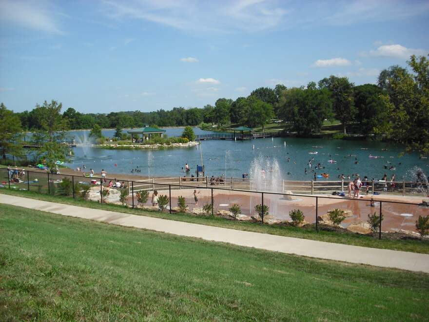 A view of Stephens Lake Park, with a spray ground in the foreground and the man-made island in the background.