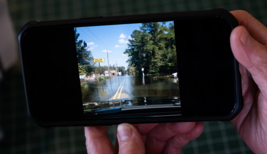 Phyllis Ellis, the owner of Johnny's Drive-In, holds a picture on Nov. 29, 2023, of the floods in downtown Fair Bluff after the hurricane in 2018. (Courtesy - Cornell Watson for WUNC)