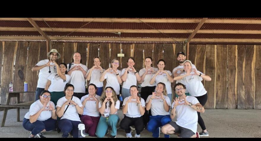 A group of 17 medical students and instructors of SIU School of Medicine in white t-shirts under a wooden low-roof shelter in costa rica. 
