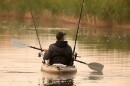 A man use an oar in his kayak with two fishing rods sticking up
