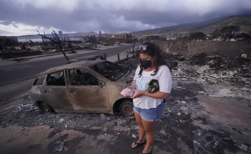 Summer Gerlingpicks up her piggy bank found in the rubble of her home following the wildfire Thursday, Aug. 10, 2023, in Lahaina, Hawaiʻi. 