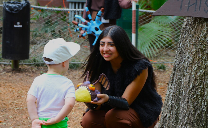 A student working at the “How to Train Your Dragon” zone at Boo at the Zoo presents a toddler with her baby dragon on Wednesday, Oct. 28, 2026. (David Caine/WUFT News)