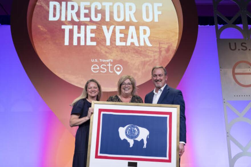Three people stand with a framed Wyoming flag, in front of a screen with a graphic that says “Director of the Year.”