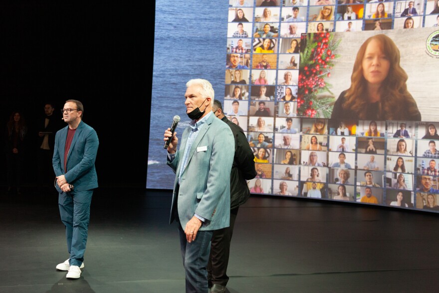 Thomas Soetens, left, and Doug Phillips, right, stand in front of a screen zoomed in on a virtual attendee.