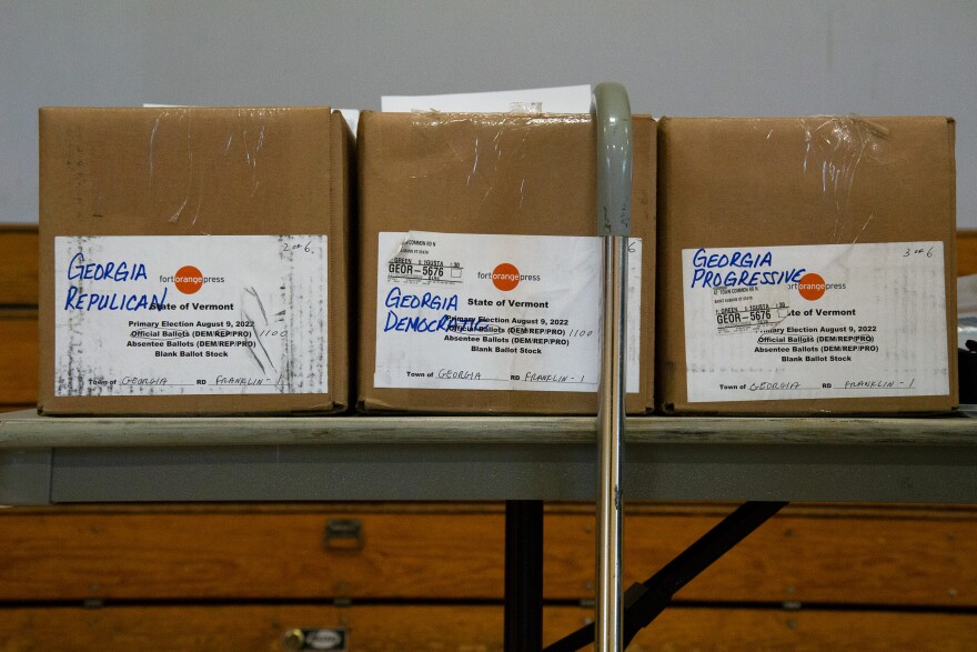 Three cardboard boxes, each labeled Georgia Republican, Georgia Democrat, Georgia Progressive, sitting on a table, with a cane hanging from the middle box