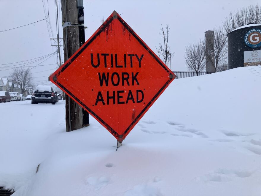 An orange sign reads "utility work ahead," and there is snow in the background. 