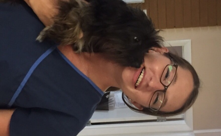 Black dog cuddle up to the face of a woman holding him.