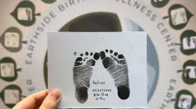 A hand is shown holding up a piece of paper showing baby ink footprints.