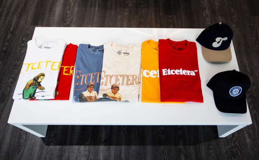 Several t-shirts with different original designs  and two fitted caps are displayed on a white coffee table.