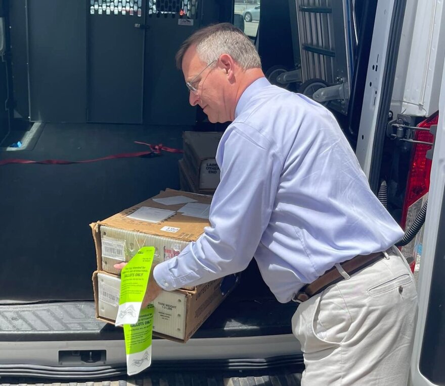 Paul Lux moves a box of vote by mail ballots.