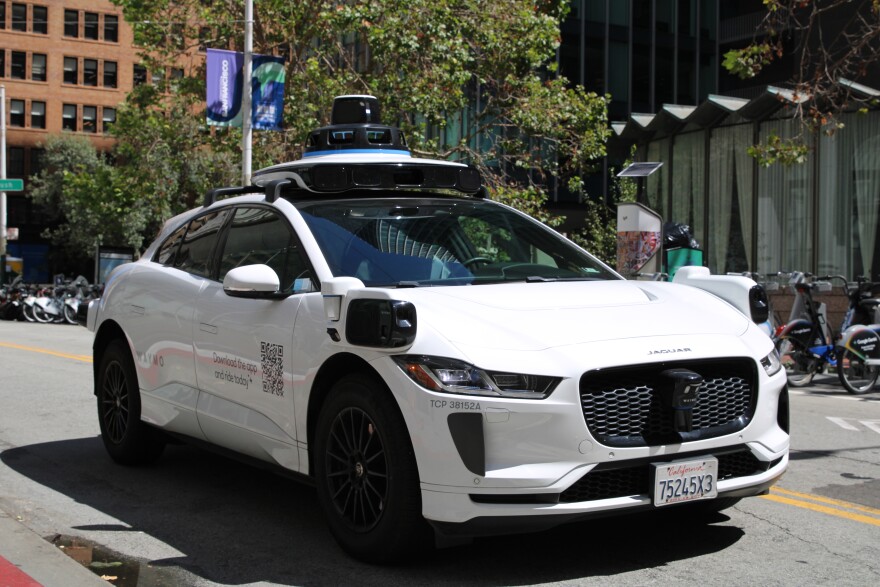 A Waymo stops at a light in San Francisco, the photo is taken from the front of the car so you can see that there is no driver, and that the car has cameras on all sides 