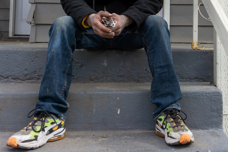 A crop of a man's legs as he sits on a gray stairway with keys in his hand.