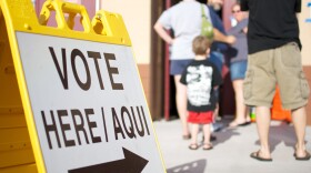 Yellow sign with VOTE HERE is standing by a line of people wating to get to the polls