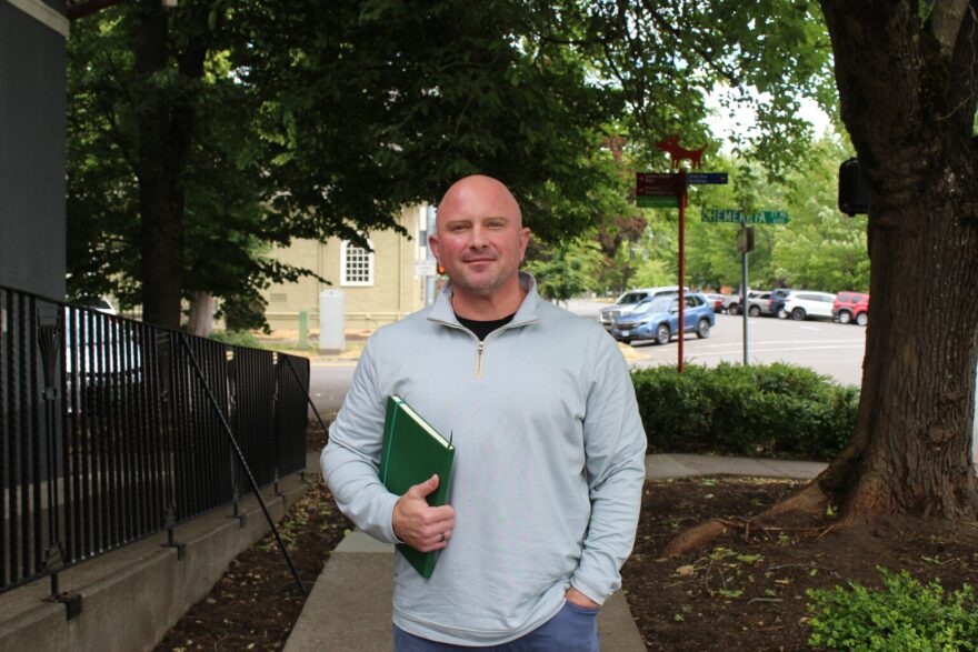 Jason Faler stands on sidewalk with a notebook under his arm.