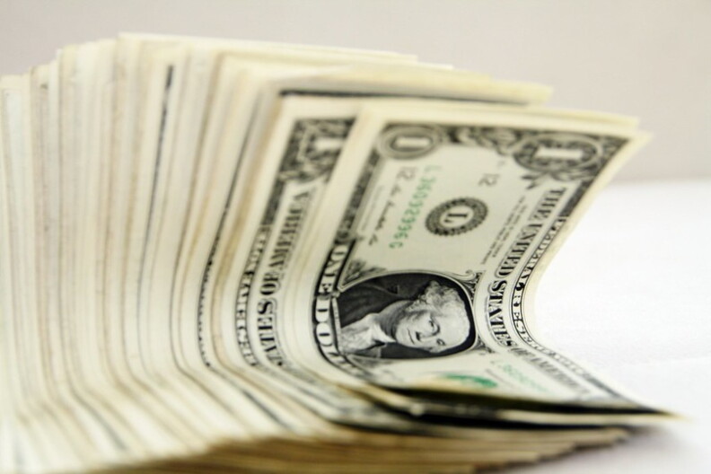 A stack of half-folded U.S. one dollar bills sit in front of a white and beige background.