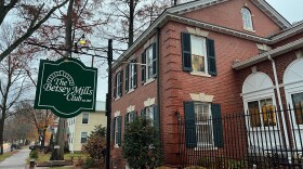 A green sign in front of a red brick building announces the Betsey Mills Club.