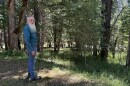 A man with a long white beard stands in a wooded area.